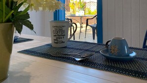 Une table avec une tasse blanche et une tasse bleue ornée d’un motif de gouvernail de navire, une plante en pot et un set de table.