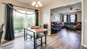 A modern living room with a large sectional sofa, a dining area with a table and chairs, and a view of the outdoors through large windows.
