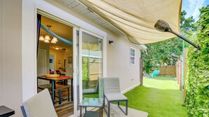 An outdoor patio with a table and chairs, a covered area with a ceiling fan, and a view of a backyard with a lawn and a wooden fence.