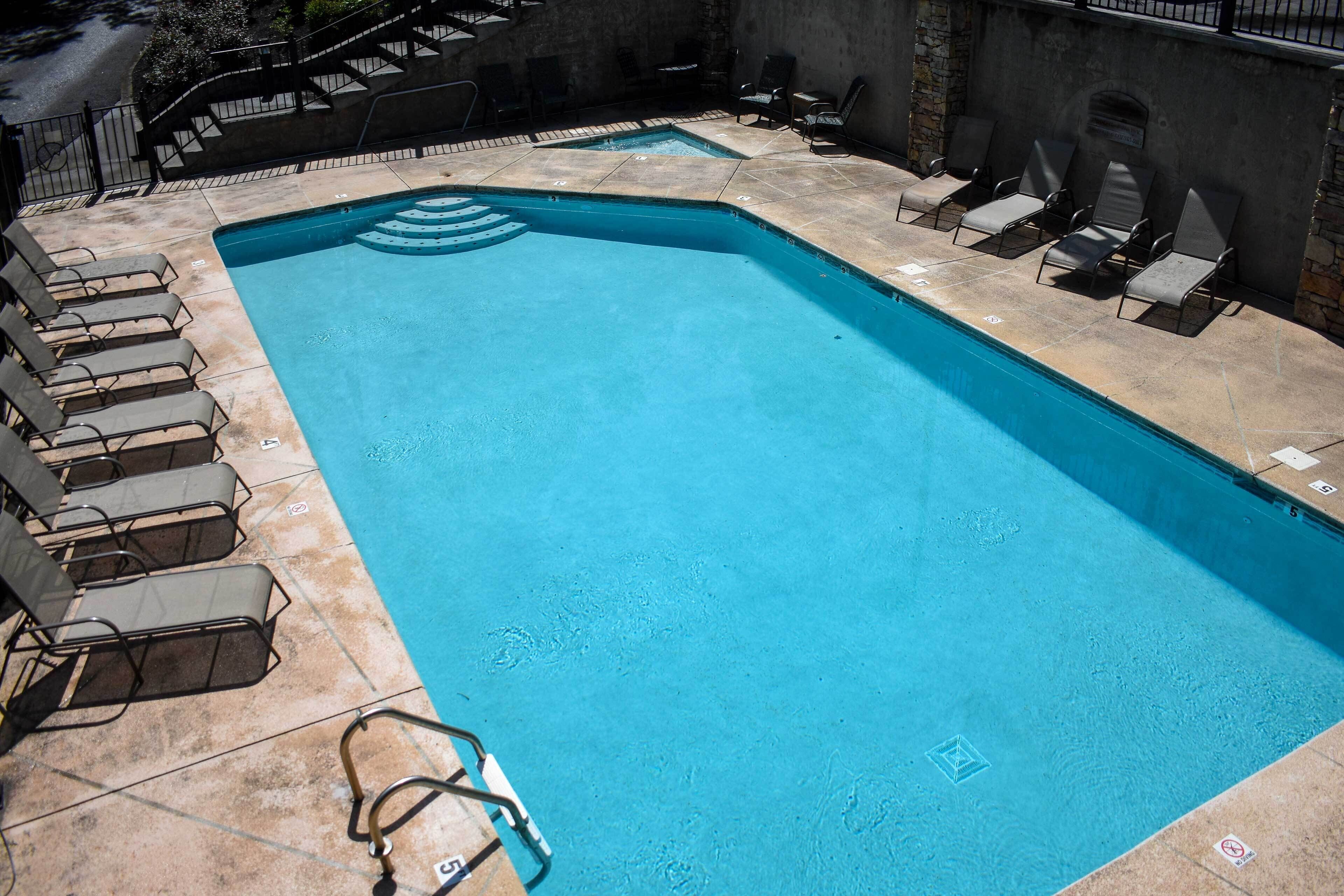 A rectangular swimming pool with a clear blue water, surrounded by lounge chairs and a stone wall.