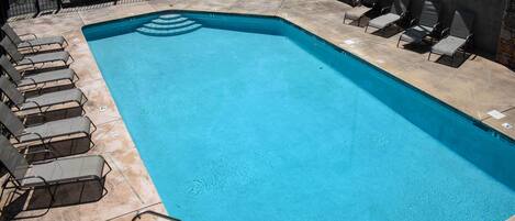 A rectangular swimming pool with a clear blue water, surrounded by lounge chairs and a stone wall.