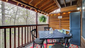 A covered outdoor seating area with a table and chairs, a potted plant, and a sign that reads "Happy." - Easy-access Pigeon Forge Cabin w/ Hot Tub! (Pigeon Forge)