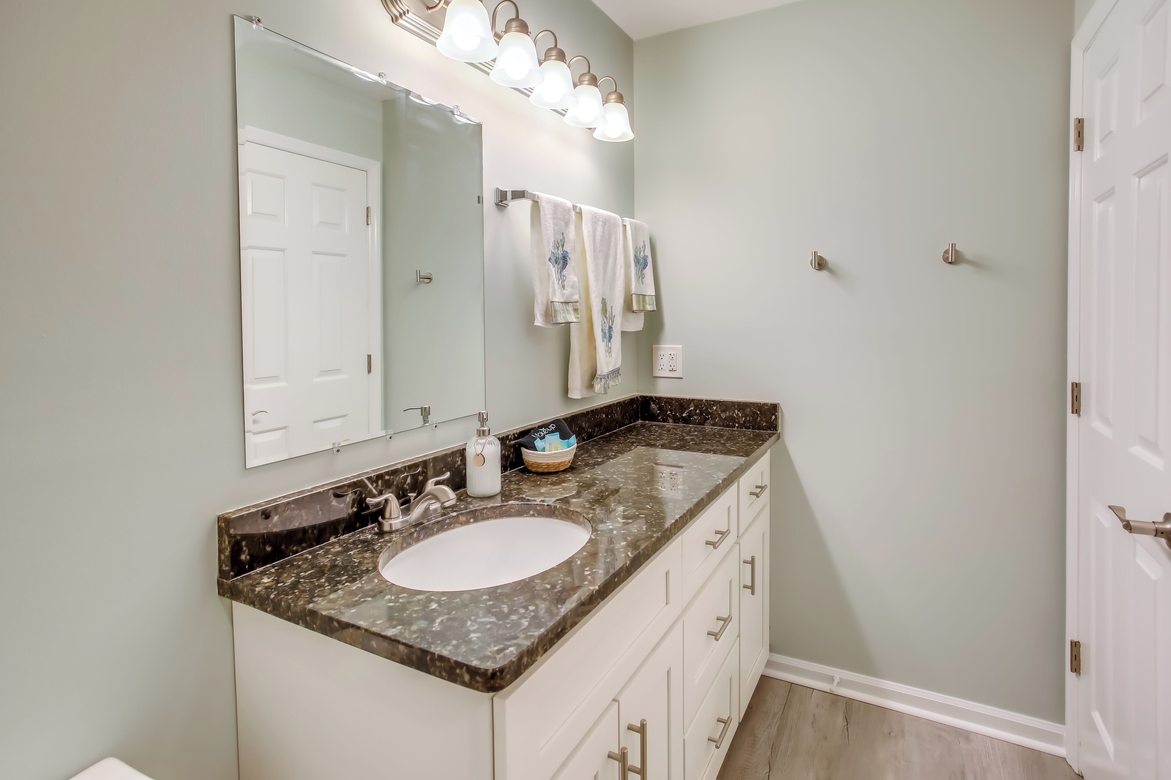 A bathroom with a marble countertop, a large mirror, and a towel rack.