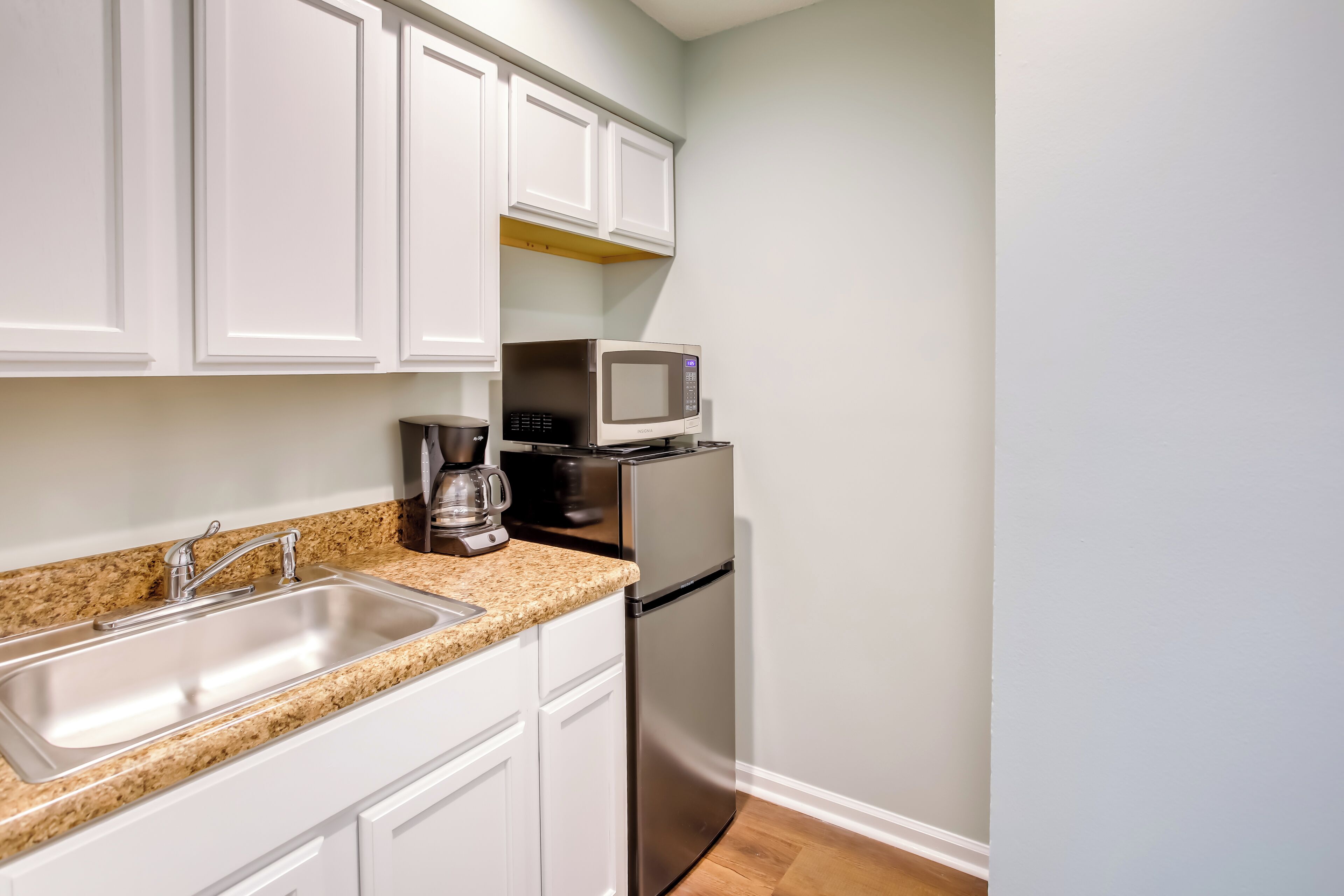 A kitchen with white cabinets, a stainless steel refrigerator, a microwave, and a coffee maker on the countertop.