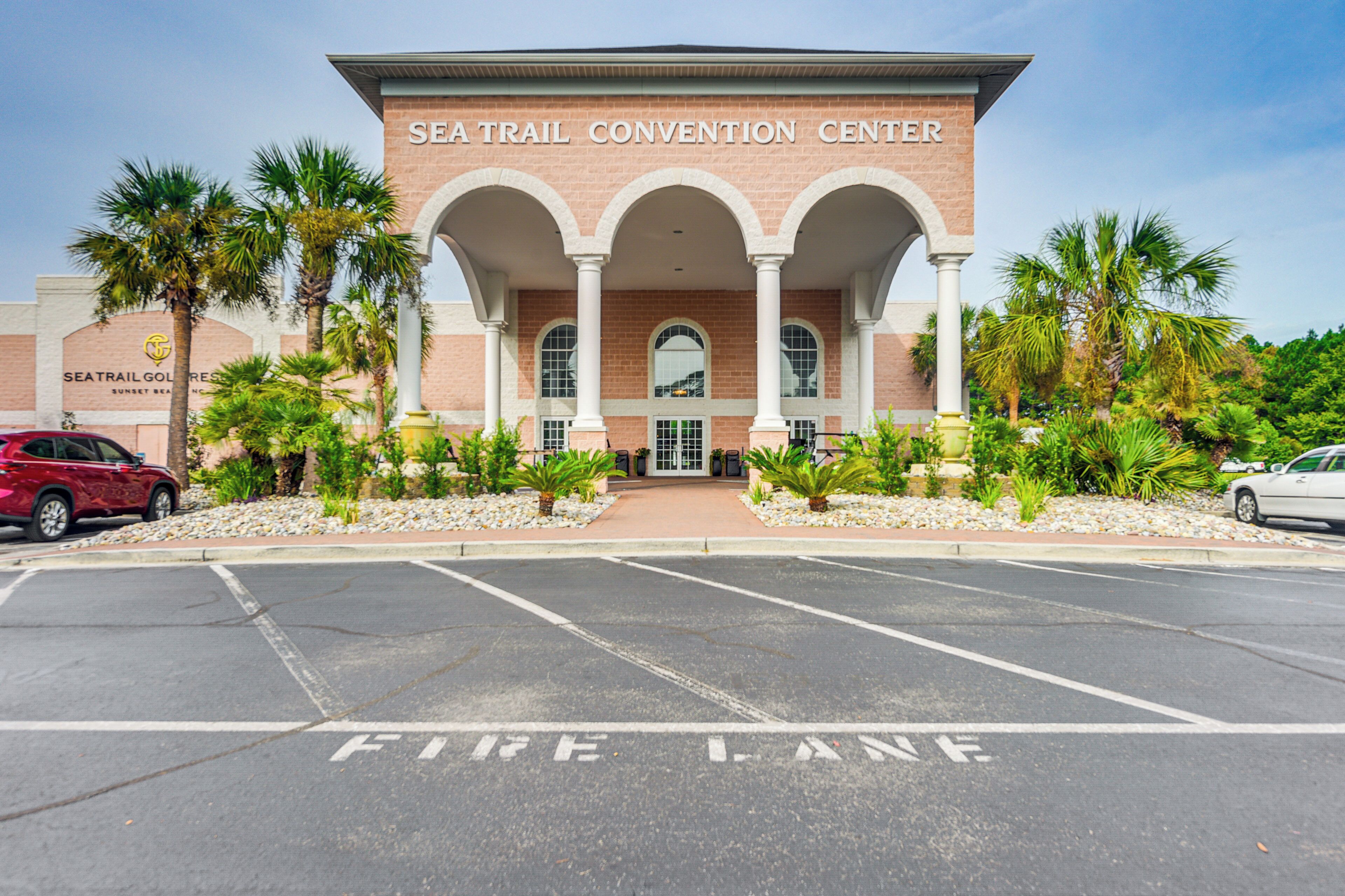 The Sea Trail Convention Center with a brick facade, arched entrance, and a parking lot with a 'Fire Lane' marking.