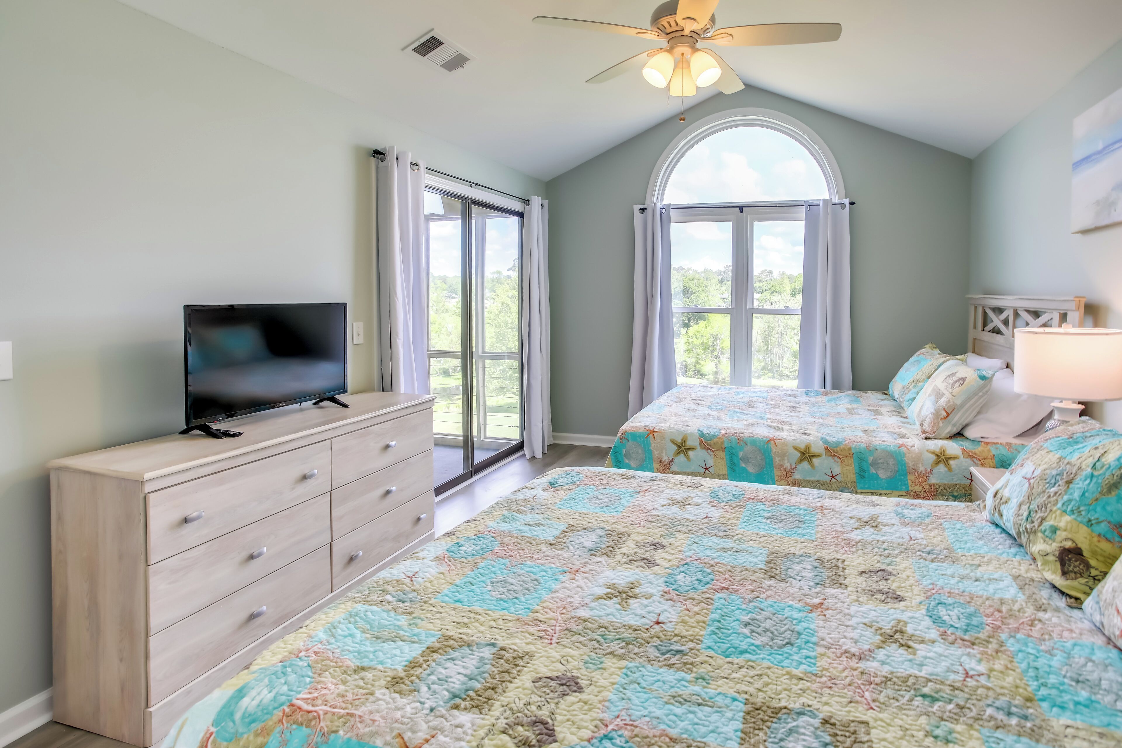 A bedroom with two beds, a TV, a dresser, and a ceiling fan.