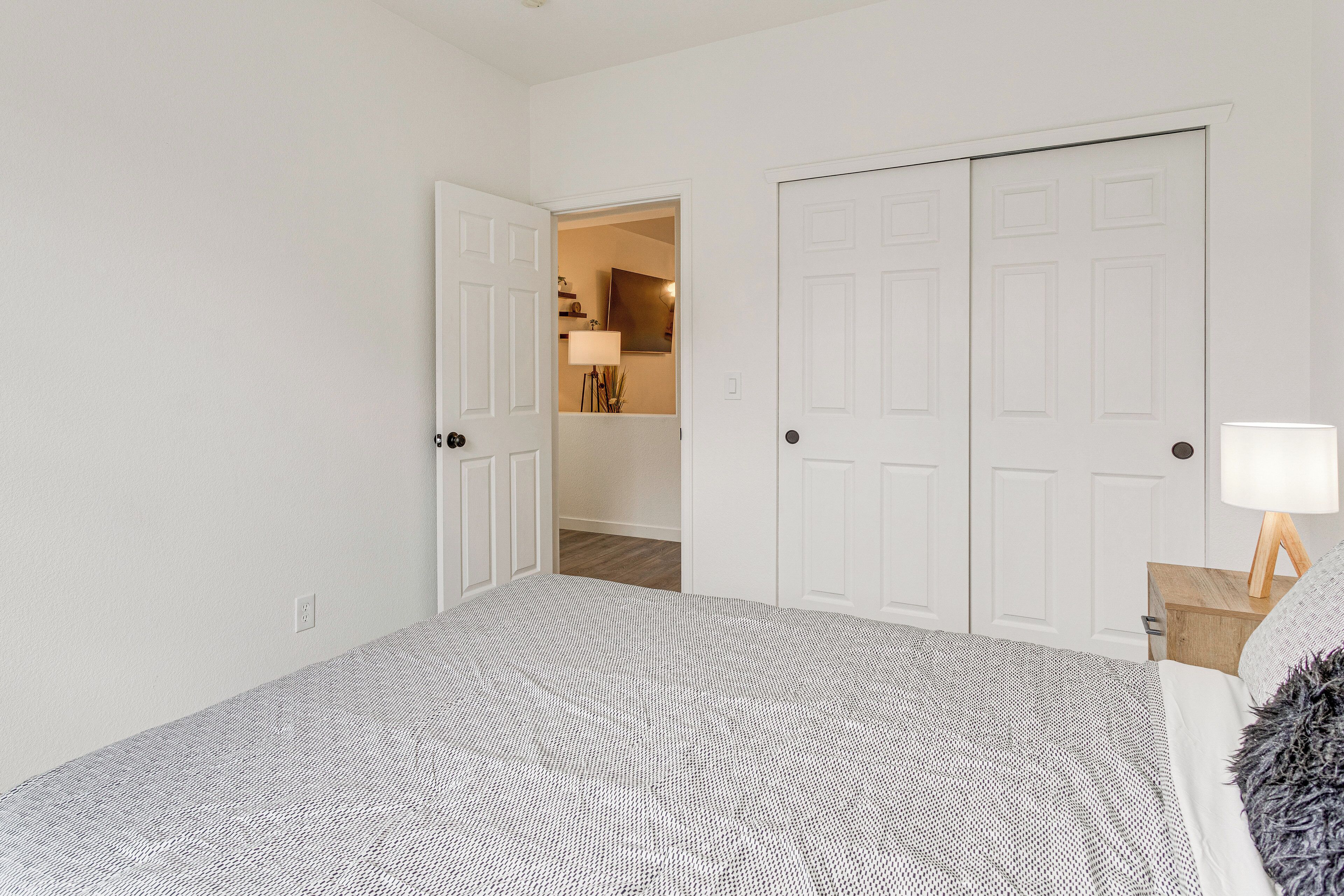 A bedroom with a large bed, white walls, and a door leading to another room.