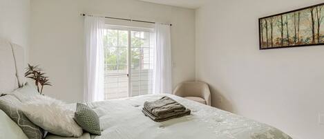 A bedroom with a bed, a chair, a window with curtains, and a painting on the wall.