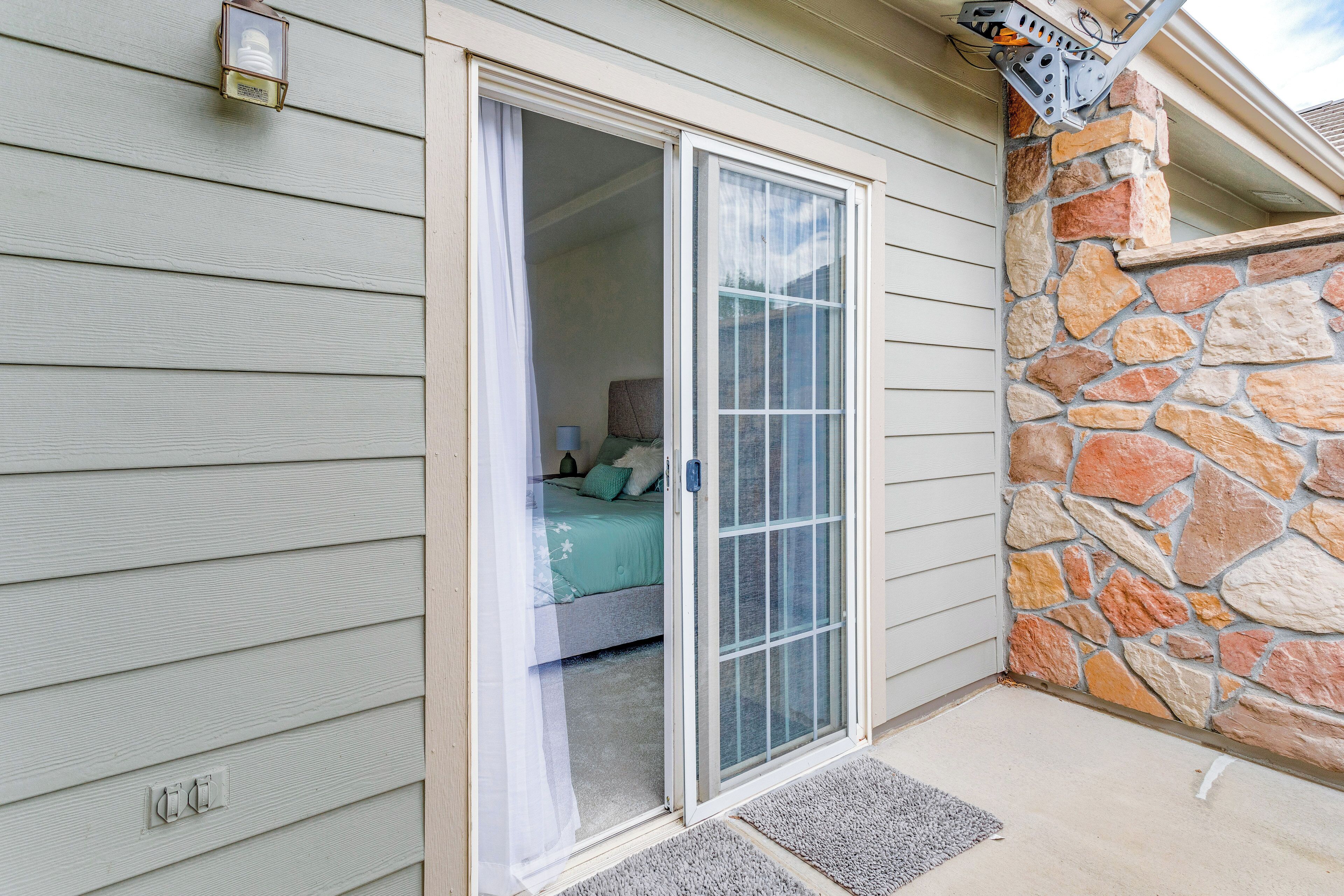 A room with a sliding glass door leading to a bedroom with a bed and a nightstand.