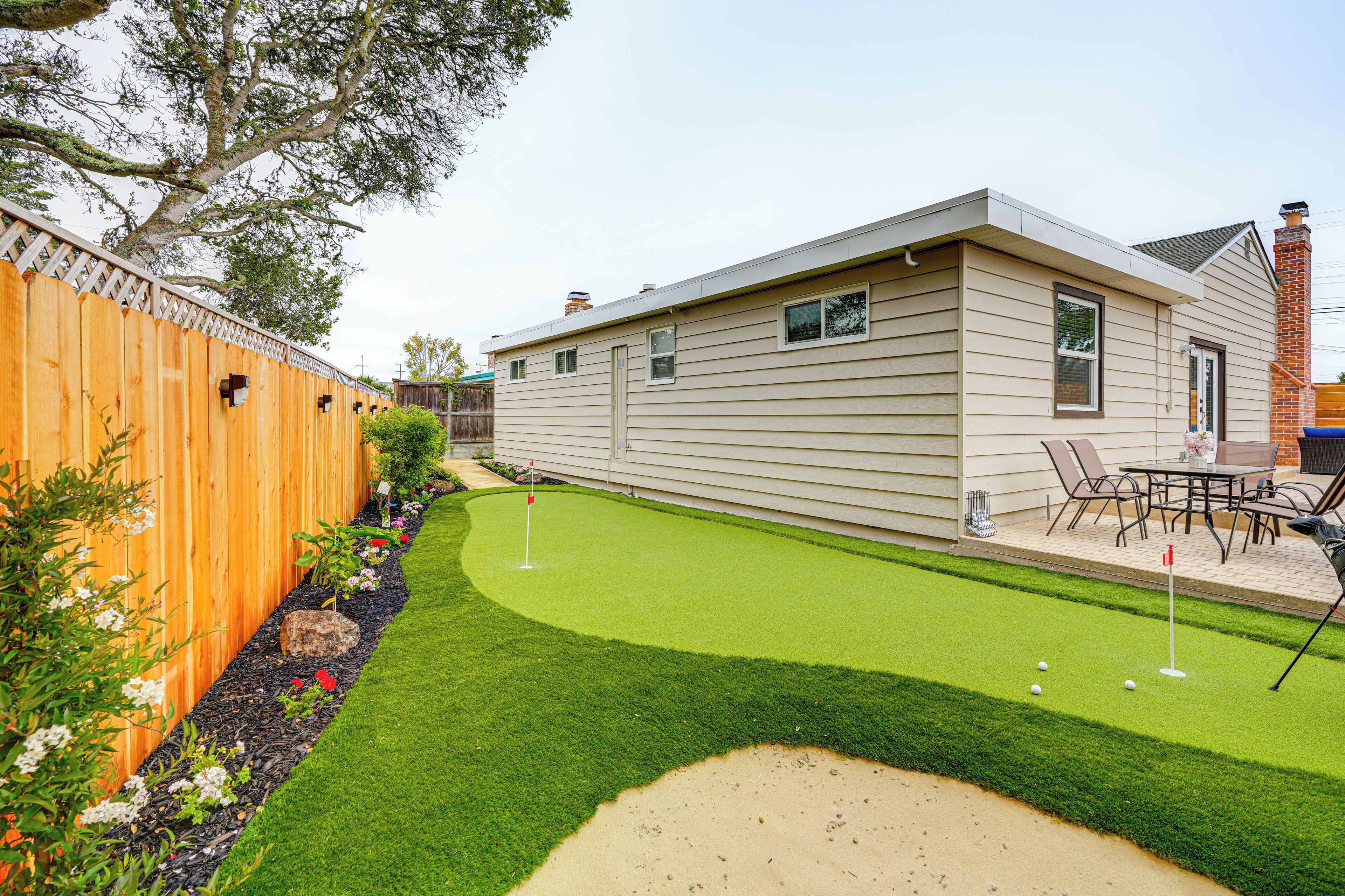 A backyard with a lawn, a wooden fence, and a house.