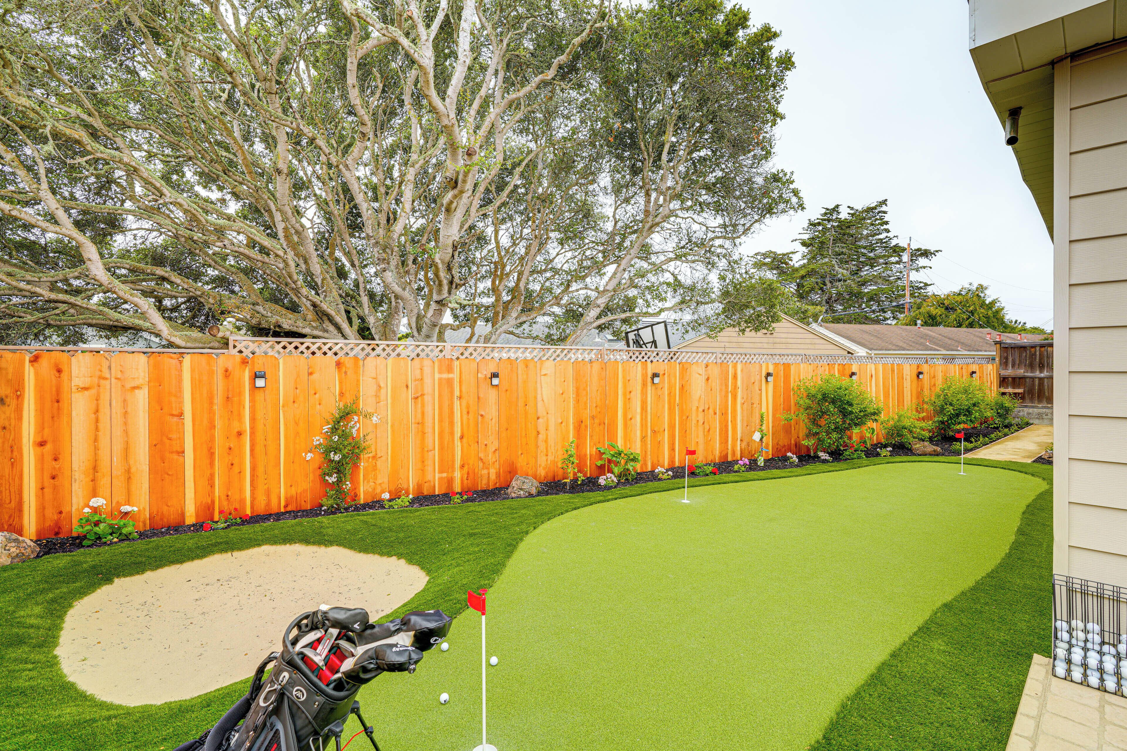 A backyard with a putting green, a sand trap, and a wooden fence.