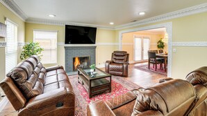 A living room with leather sofas, a glass coffee table, a fireplace, and a television. - Del Rey Oaks Vacation Home w/ Mini-golf Course! (Monterey)