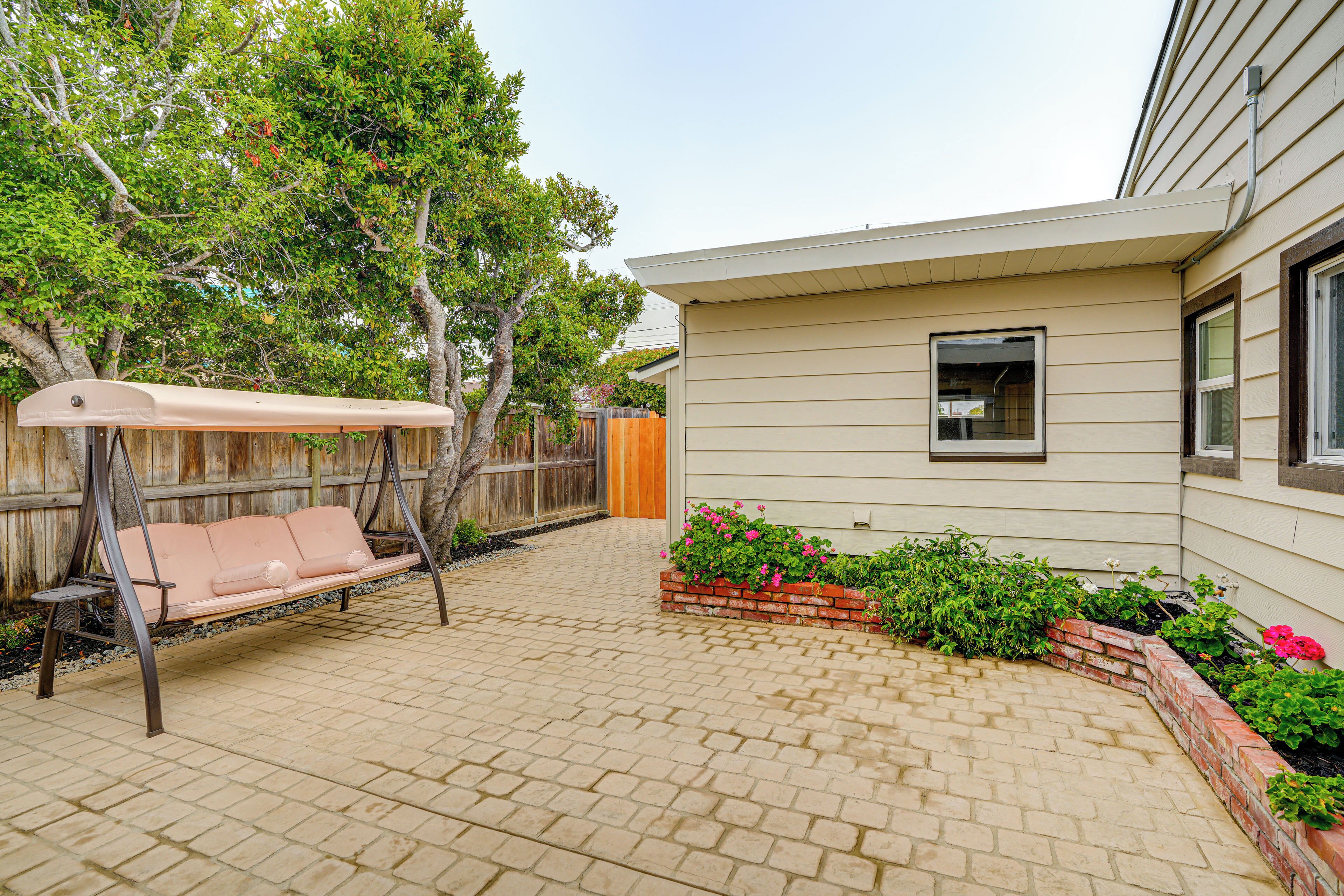A backyard with a swing set, a brick patio, and a wooden fence.