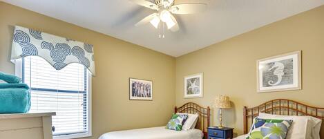 A bedroom with two beds, a ceiling fan, and a window with blinds.
