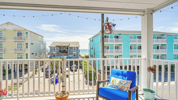 A balcony with a blue chair, a potted plant, and a view of neighboring buildings. - Carolina Beach Condo w/ Balcony: Walk to the Ocean (Carolina Beach)