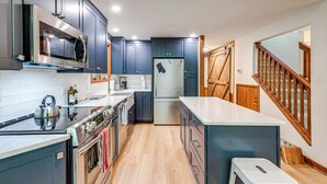 A modern kitchen with dark cabinets, stainless steel appliances, and a wooden staircase. - Creek Access & Deck: Family Pocono Pines Cottage (Pocono Pines)