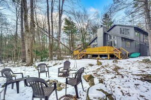 A cabin with a deck, surrounded by snow-covered ground and trees.