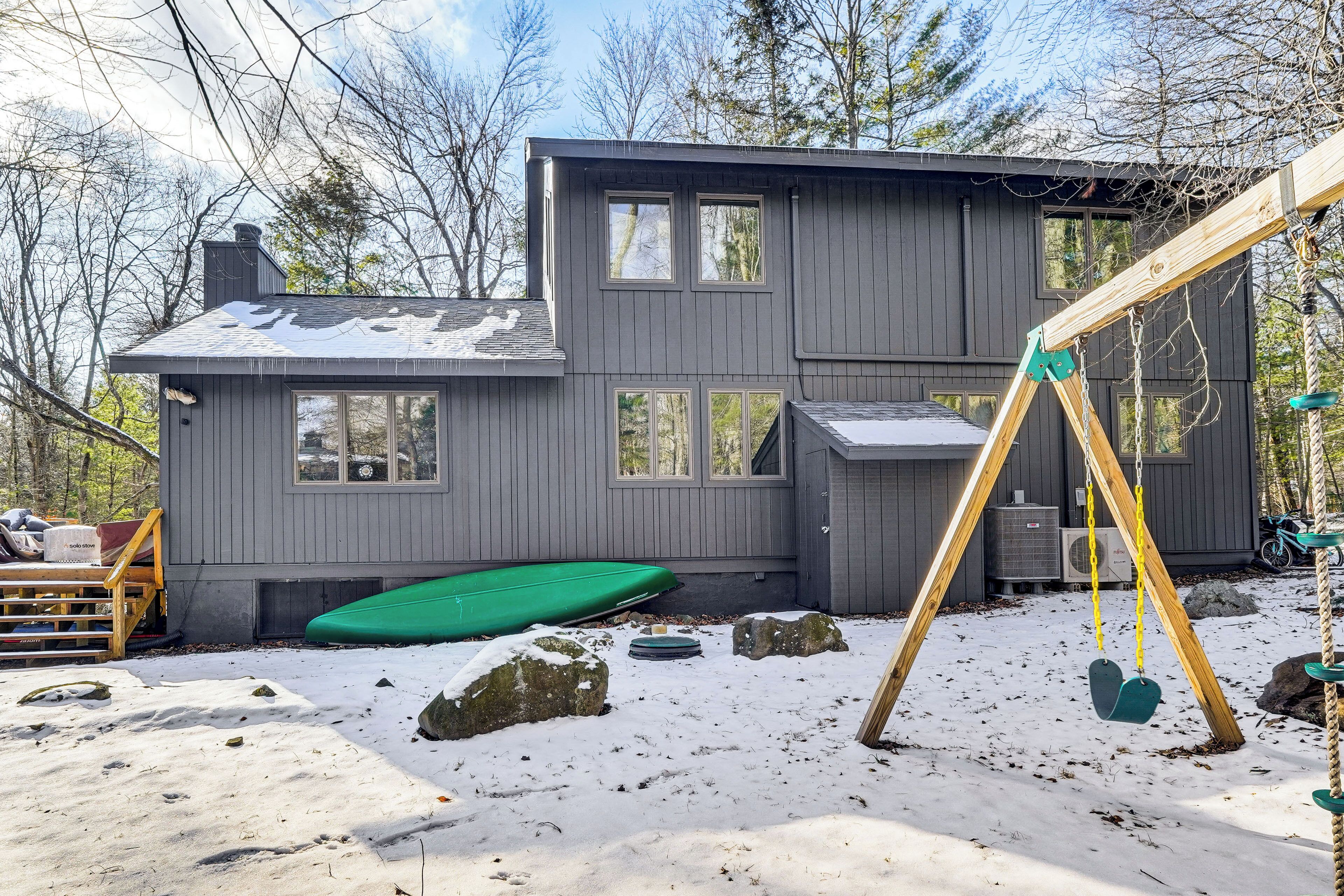 A two-story house with a wooden deck and a swing set.