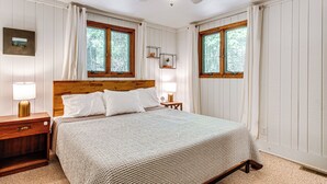 A neatly arranged bedroom with a wooden headboard, two bedside tables with lamps, a bed with white bedding, and two windows with curtains. - Creek Access & Deck: Family Pocono Pines Cottage (Pocono Pines)