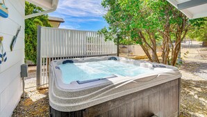 Een hottub met een houten terras en een witte omheining in een achtertuin.