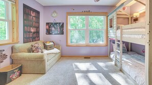 A cozy room with a bunk bed, a sofa, a bookshelf, and a large window.