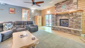 A living room with a stone fireplace, leather sofa, and a ceiling fan.