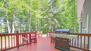 A wooden deck with a barbecue grill, surrounded by trees and a house.