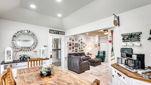 A modern kitchen with a coffee station, a dining area with a wooden table, and a living room with a gray sofa and green armchair. - Home on Lake Granbury w/ Hot Tub: 5 Mi to Dtwn! (Granbury)