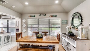 A dining area with a wooden table, chairs, and a bench. There are decorative fish wall art, a mirror, and a sign on the wall. - Home on Lake Granbury w/ Hot Tub: 5 Mi to Dtwn! (Granbury)