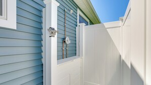 A white wooden gate, a metal gate latch, and a metal pipe against a blue siding house. - Old Saybrook Home w/ Screened Porch & Ocean View! (Old Saybrook)