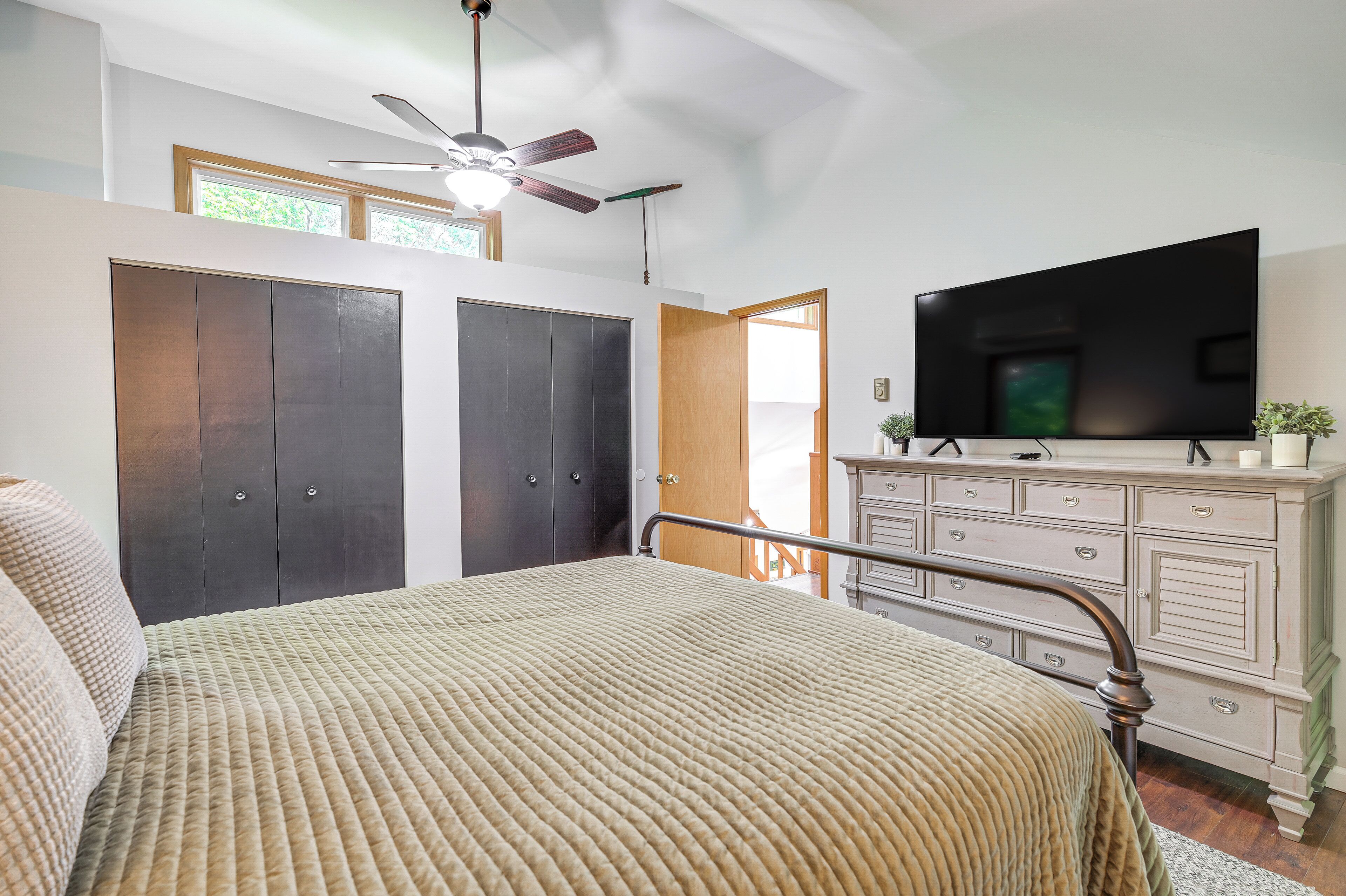 Un dormitorio con cama, cómoda, televisor y ventilador de techo.