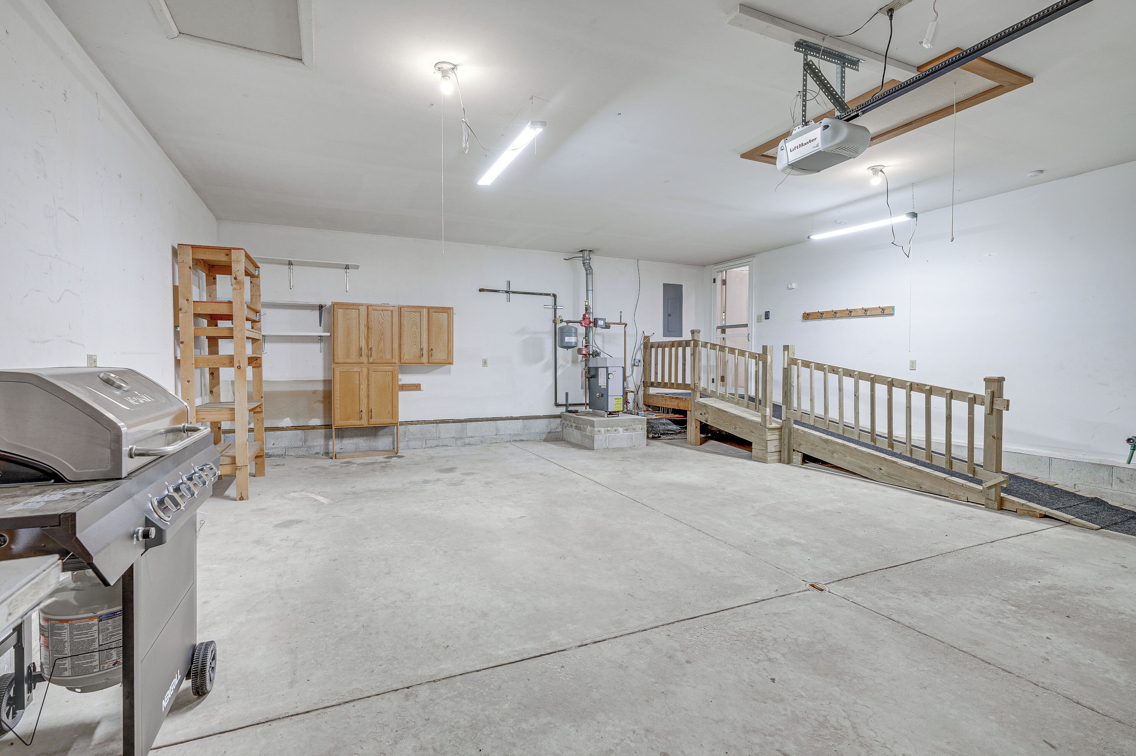 A spacious garage with a concrete floor, a wooden staircase, and a barbecue grill.