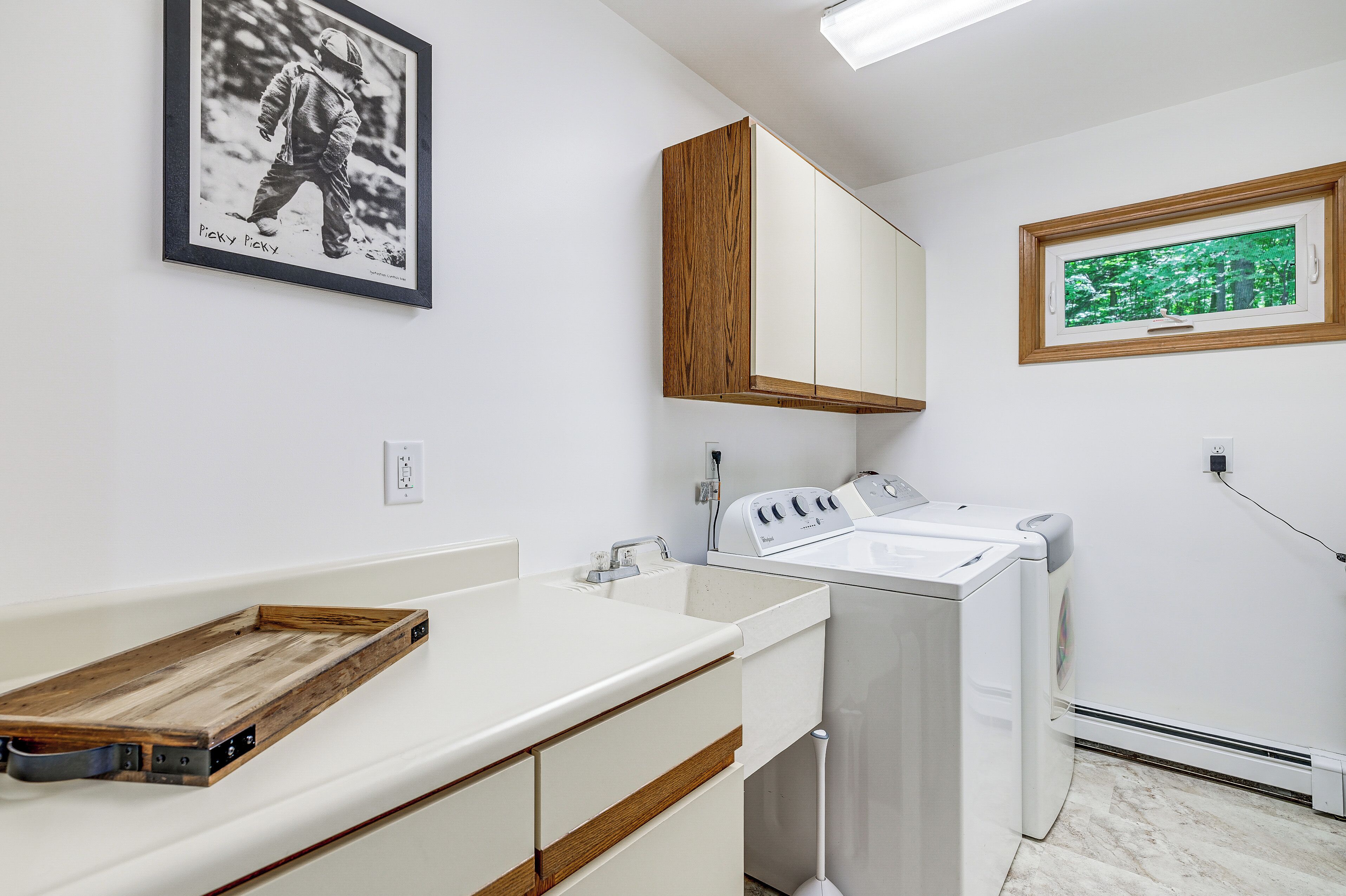 A modern bathroom with a wooden vanity, a built-in washing machine, and a framed photograph on the wall.