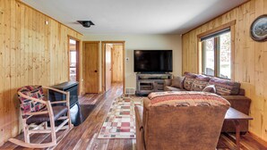 A cozy living room with wooden walls, a television, a sofa, and a rocking chair. - Updated Conover Cabin w/ Nearby Boating Access! (Conover)