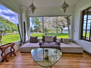 Ein modernes Wohnzimmer mit einem großen Fenster, einem Glastisch und einem beige farbenen Sofa mit vielen Kissen.