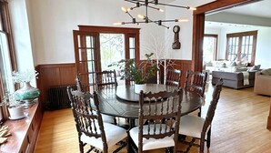 Een eetruimte met een ronde tafel, omringd door houten stoelen, een kroonluchter en potplanten.