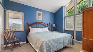 A bedroom with a large bed, a wooden chair, a nightstand, and a window with blinds. - Boyne Mountain Cozy Winter Cabin!  Sleeps 6!  Right at base of Mountain (Boyne Falls)
