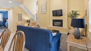 A living room with a blue sofa, wooden chairs, a fireplace, a TV, and a staircase. - Boyne Mountain Cozy Winter Cabin!  Sleeps 6!  Right at base of Mountain (Boyne Falls)