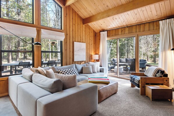 A spacious living room with a large sofa, a small wooden table, and a view of the outdoors through large windows.