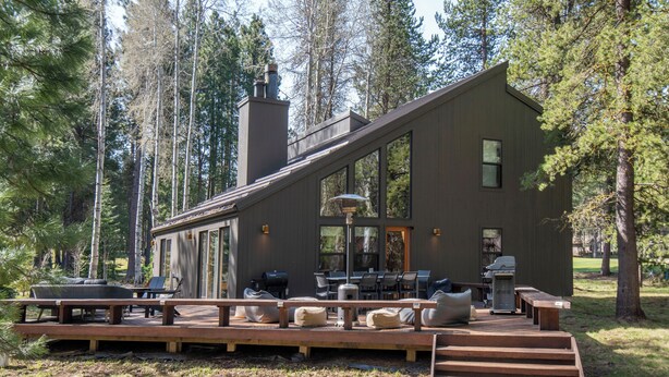 Una cabaña moderna con terraza, mobiliario exterior y chimenea.