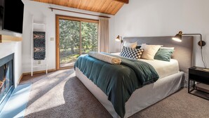 Un dormitorio con cama, televisión, chimenea y un ventanal grande.