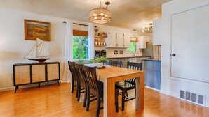 A modern kitchen with white cabinets, a dining area with a wooden table and chairs, and a small sailboat model on a cabinet. - Chirping Pines: Modern Lake Home on Cayuga Lake (Seneca Falls)