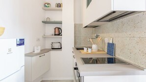 Een moderne keuken met witte kasten, een ingebouwde oven, een rvs-afzuigkap en een aanrecht met waterkoker en broodrooster.