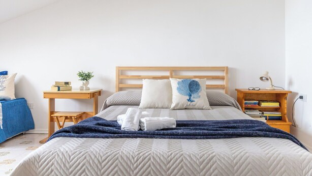 Een slaapkamer met een bed, nachtkastje, leeslamp en een boekenplank.