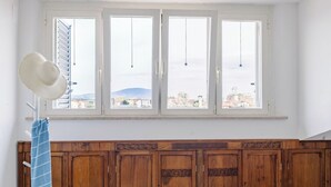 Een kamer met een groot raam, een houten garderobe en een hoed op een standaard.