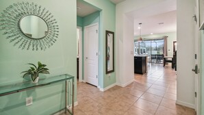 A hallway with a glass railing, a potted plant, a sunburst mirror, and a dining area with a table and chairs.