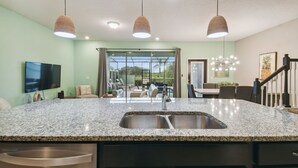 A kitchen with granite countertops, stainless steel sink, and pendant lights.