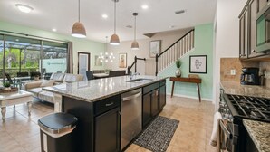 A spacious kitchen with granite countertops, a dishwasher, and a stove. There is a dining area with a table and chairs, and a staircase leading to another level.