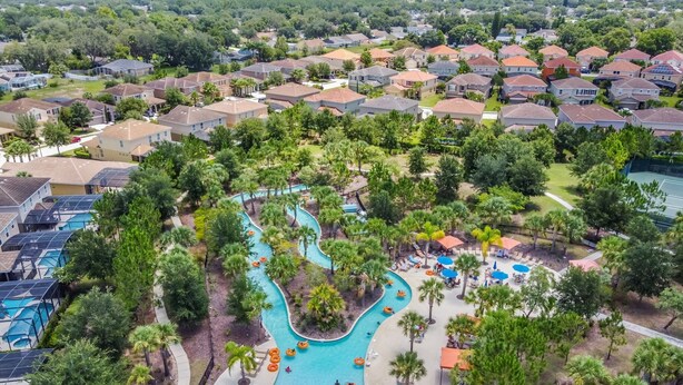 An aerial view of a residential area with a winding pool surrounded by palm trees and a small park area with lounge chairs.