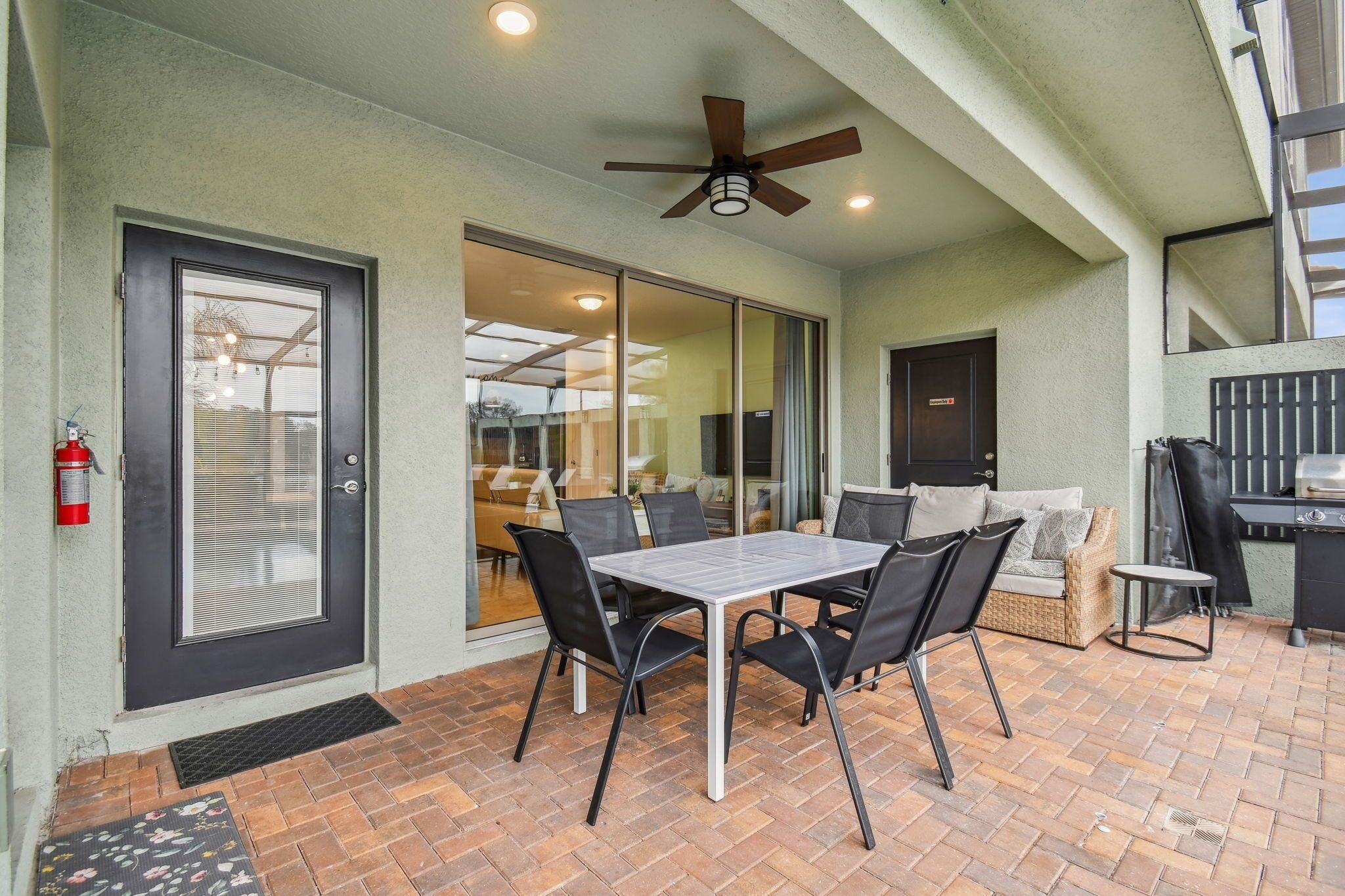 A patio area with a table and chairs, a ceiling fan, and a sliding glass door leading to an indoor space.